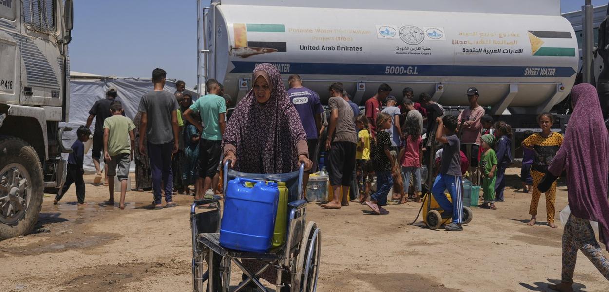 Palestinka gura invalidska kolica u kojima se nalaze plastični kanisteri s vodom, u kampu za raseljene osobe u Kan Junisu, na jugu Pojasa Gaze, 19. jul 2025. (Foto: AP Photo/ Abdel Kareem Hana)