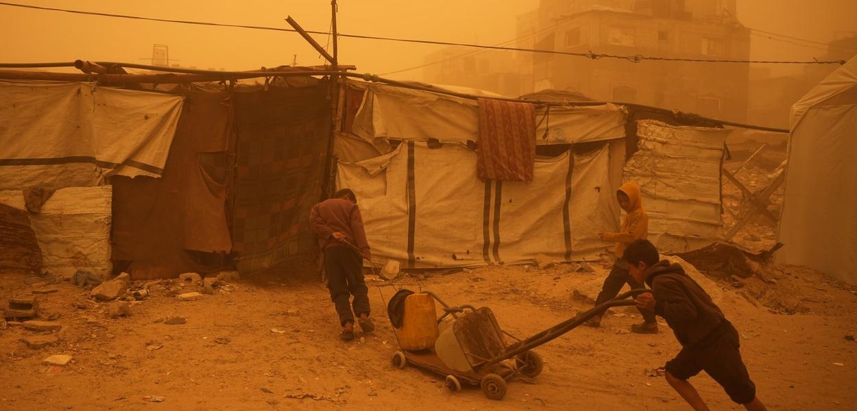Palestinska djeca nose plastične posude napunjene vodom kroz pješčanu oluju u Han Junisu, južni pojas Gaze (Foto: AP foto/Abdel Kareem Hana)