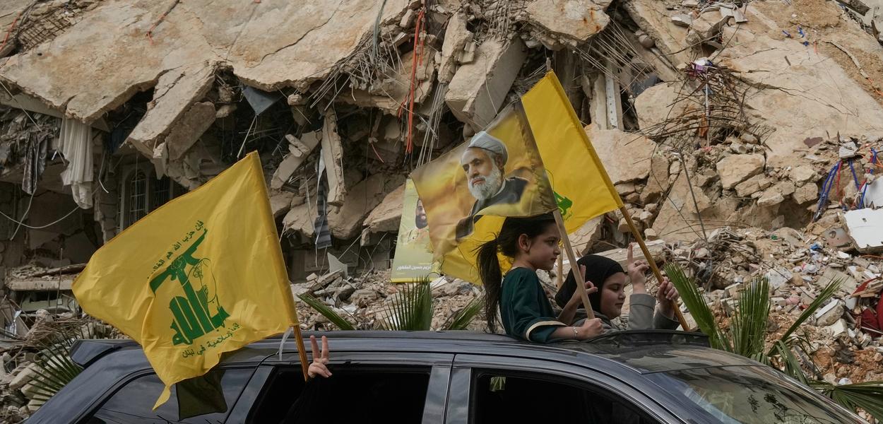 Raseljeni stanovnici mašu zastavama Hezbolaha, uključujući i jednu sa slikom njegovog lidera Naima Kasema, dok prolaze pored ruševina uništenih zgrada u Dahijehu, južnim predgrađima Bejruta, Liban, u petak, 17. aprila 2026. godine, nakon primirja između Izraela i Hezbolaha (Foto: AP foto/Bilal Hussein)